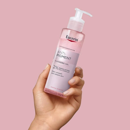 Hand holding a bottle of Eucerin Anti-Pigment Cleansing Gel against a pink background