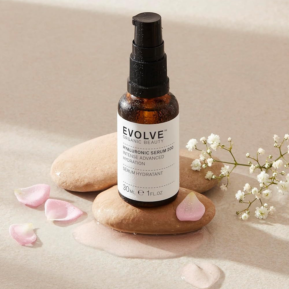Skincare serum bottle labeled 'Evolve' on stones with flowers and petals.