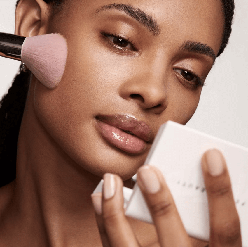 Model applying Fenty Beauty Mini Invisimatte Setting Powder with a brush for a flawless finish.