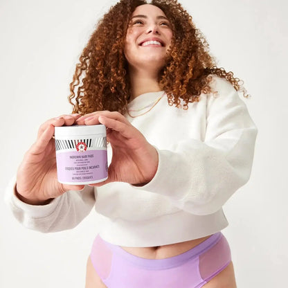 Smiling woman holding First Aid Beauty Ingrown Hair Pads jar, showcasing skincare product for ingrown hair treatment.