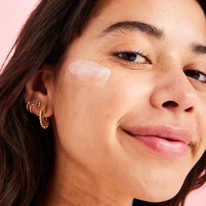 Close-up of a model applying First Aid Beauty Coconut Skin Smoothie Priming Moisturiser, showcasing its smooth texture.