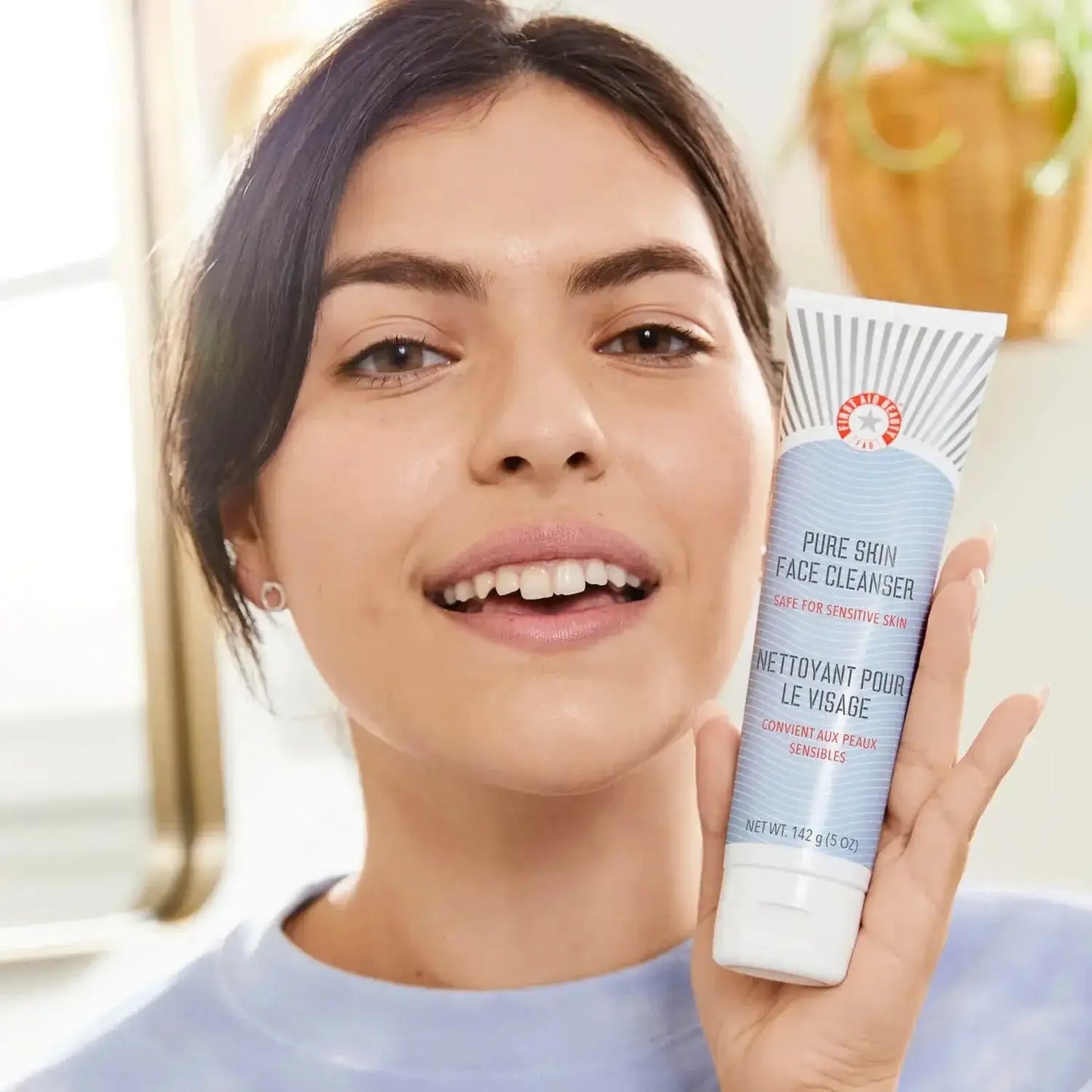 First Aid Beauty Face Cleanser 142g for sensitive skin, woman holding product, promoting healthy skin and cleansing.