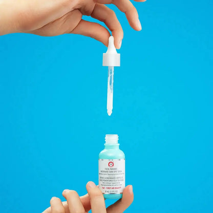 First Aid Beauty Facial Radiance Niacinamide Dark Spot Serum 28.3g with dropper against a blue background.