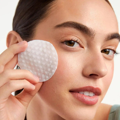 Model holding First Aid Beauty Facial Radiance Pad to her cheek for gentle exfoliation.