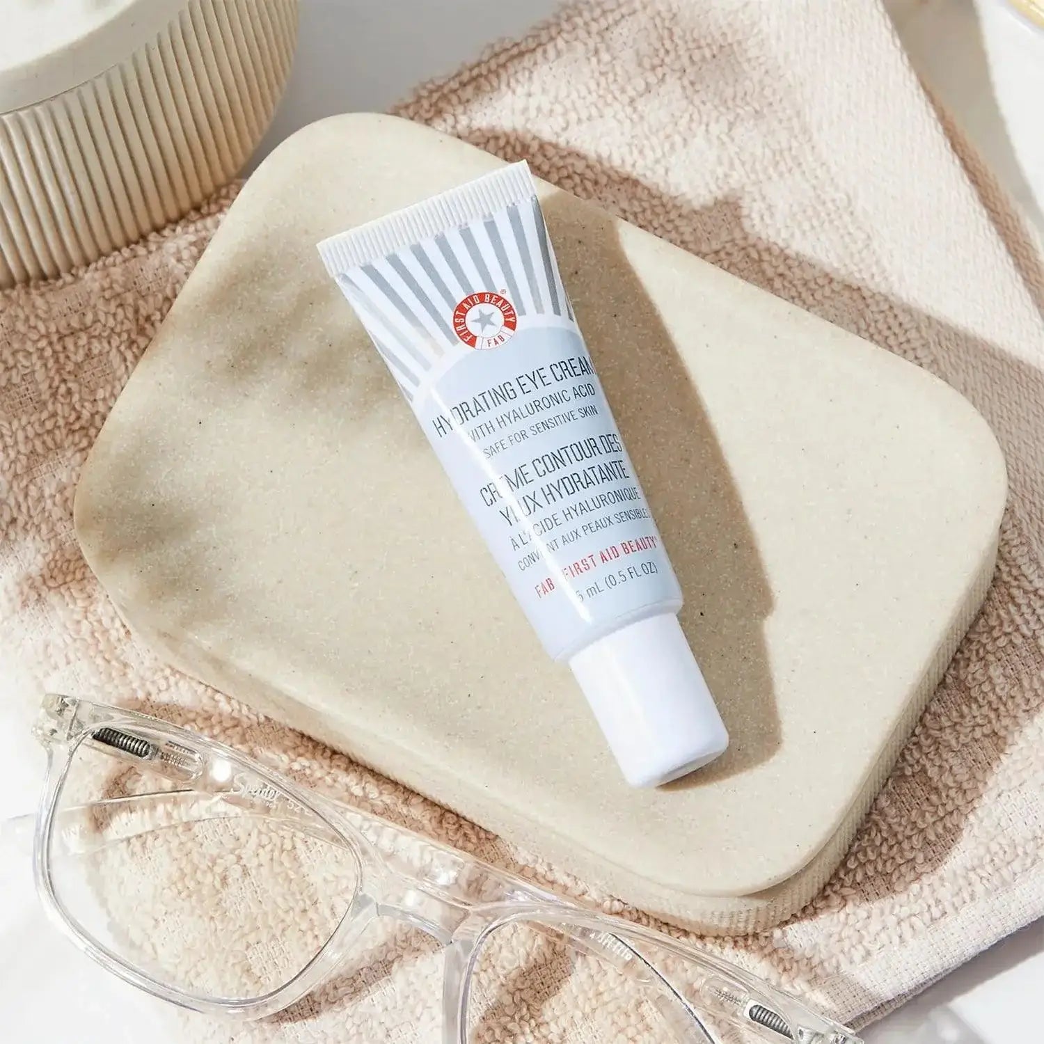 First Aid Beauty Hydrating Eye Cream 15ml tube on a beige plate, designed to moisturize and reduce puffiness.