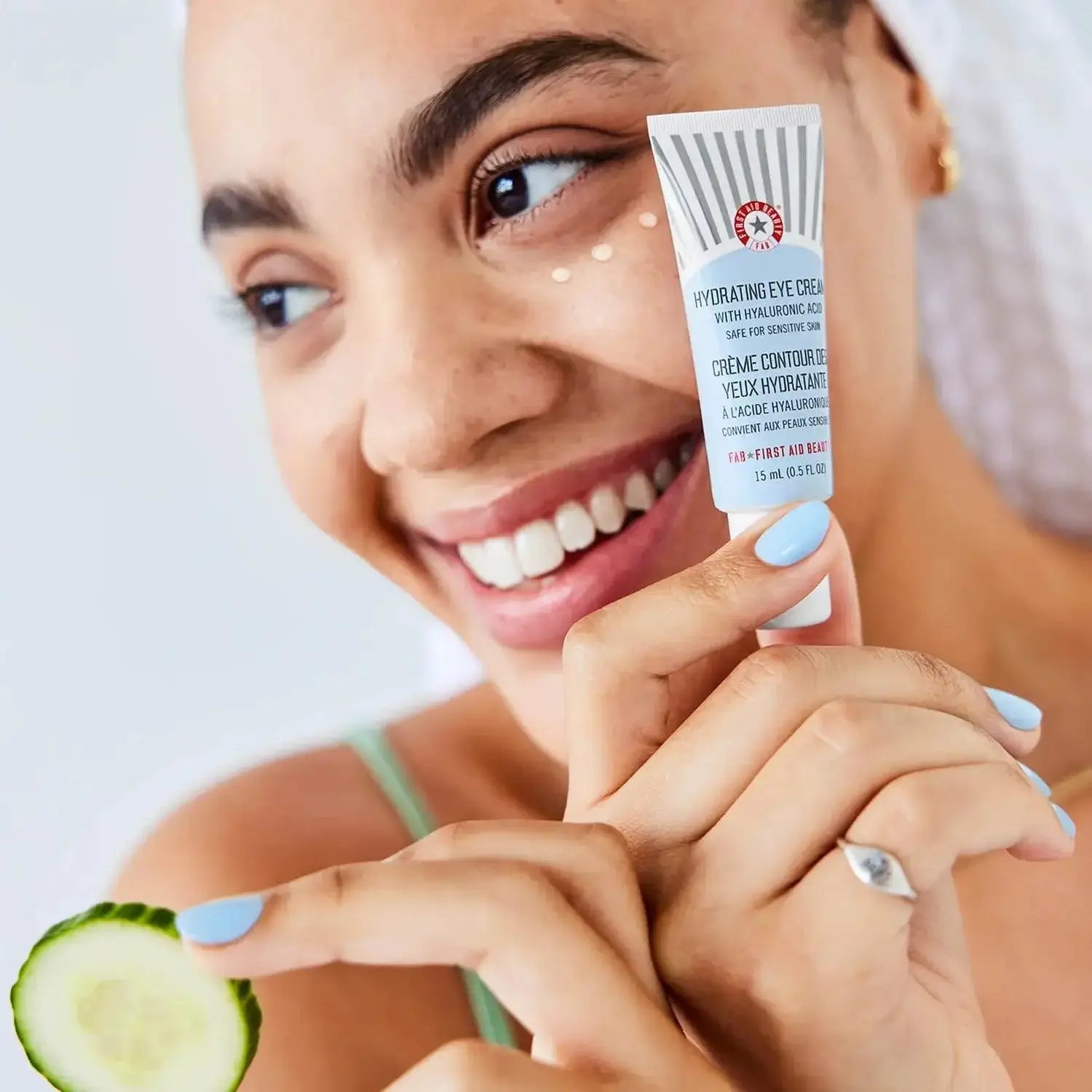 First Aid Beauty Hydrating Eye Cream 15ml held by a smiling woman, showcasing its hydrating benefits with cucumber.
