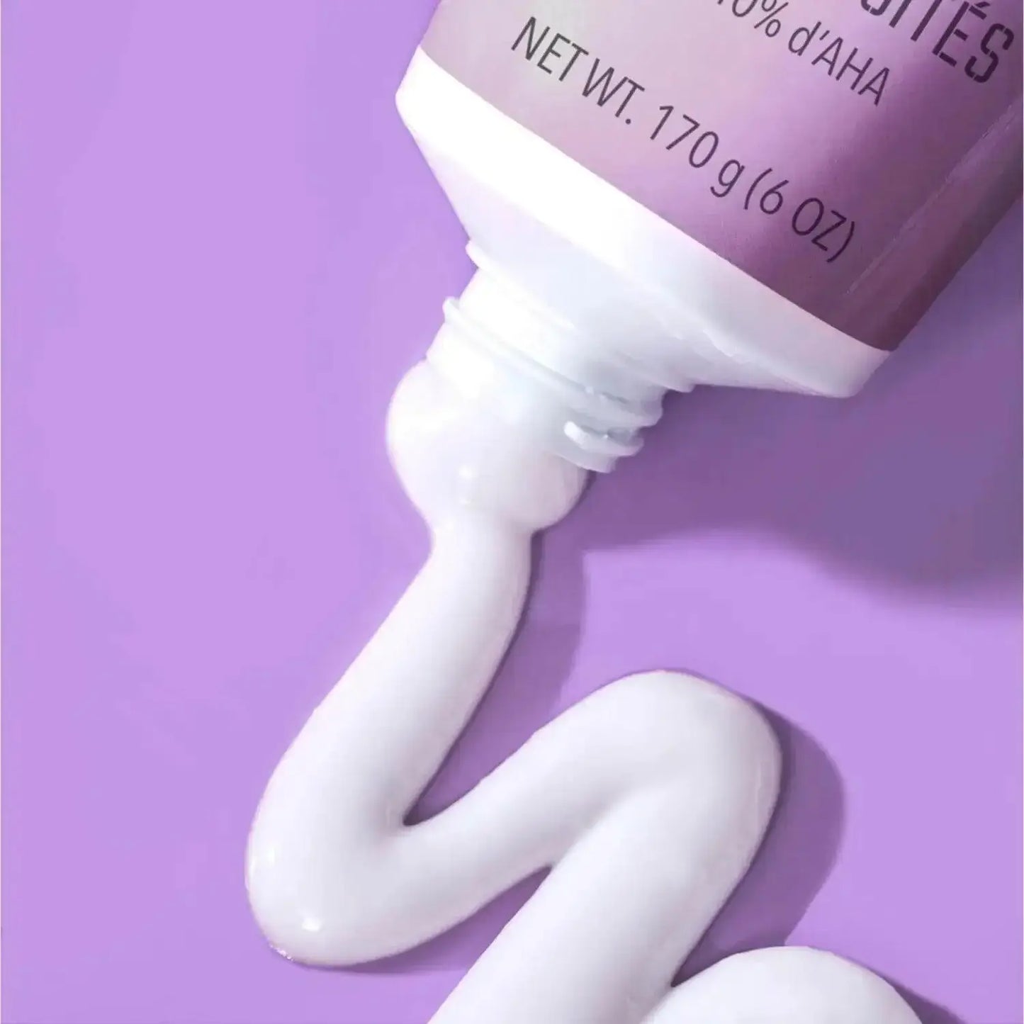 First Aid Beauty KP Smoothing Body Lotion with 10% AHA squeezed from a tube against a purple background.