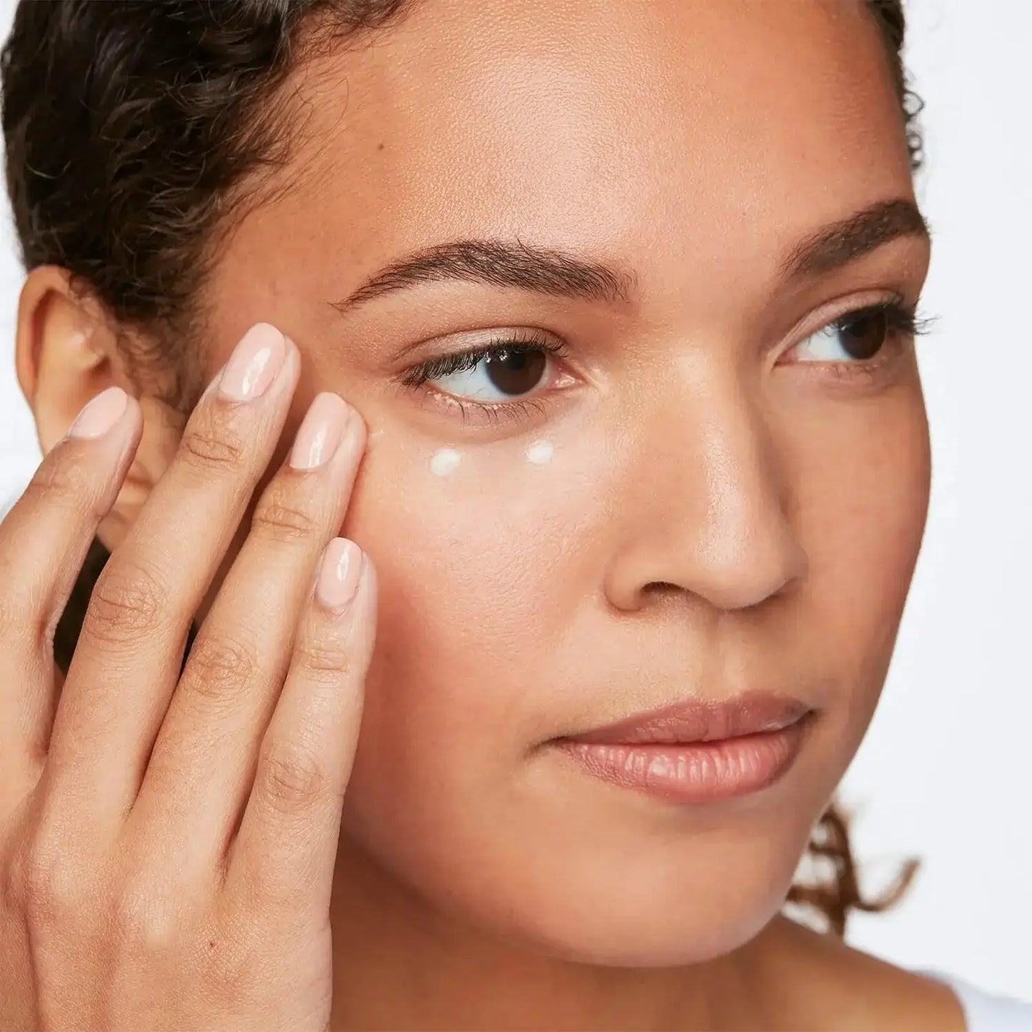 Close-up of a woman applying First Aid Beauty Skin Lab Retinol Eye Cream under her eye for rejuvenation.