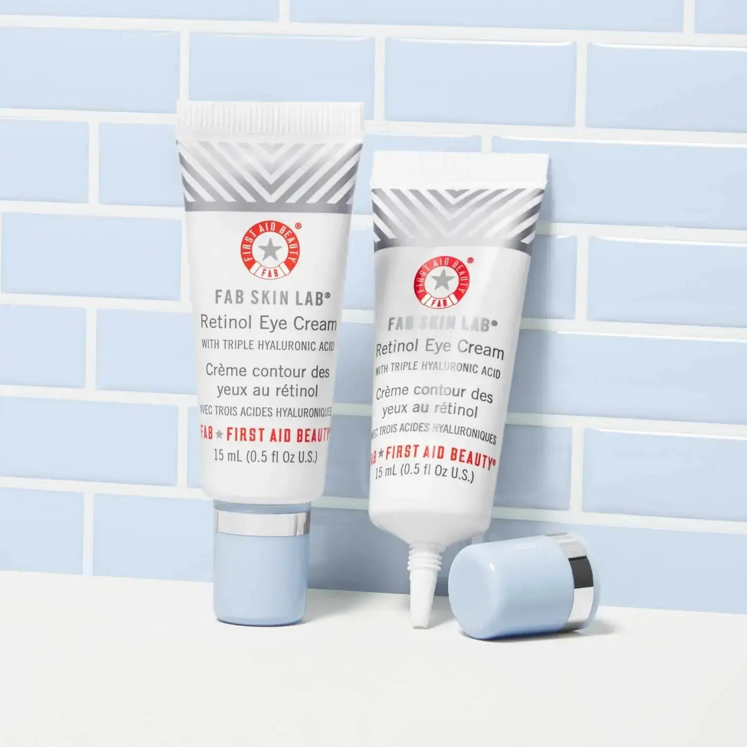 First Aid Beauty Skin Lab Retinol Eye Cream with Triple Hyaluronic Acid 15ml in a sleek tube on a blue tile background.