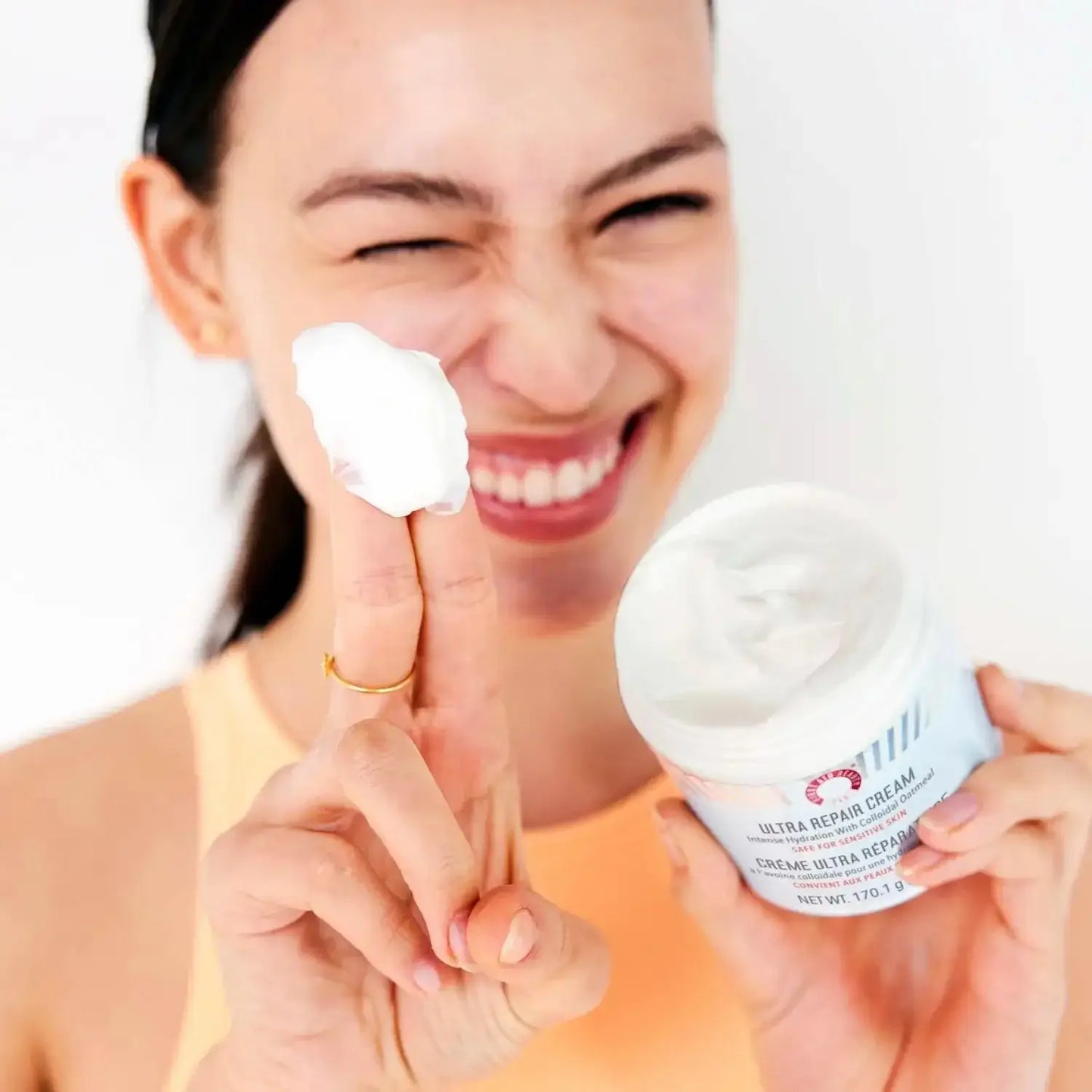 Person holding First Aid Beauty Ultra Repair Cream 170g with a dollop on finger, showcasing its rich texture.