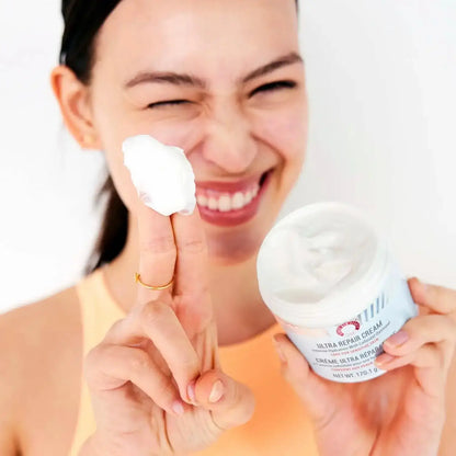 Person holding First Aid Beauty Ultra Repair Cream 170g with a dollop on finger, showcasing its rich texture.