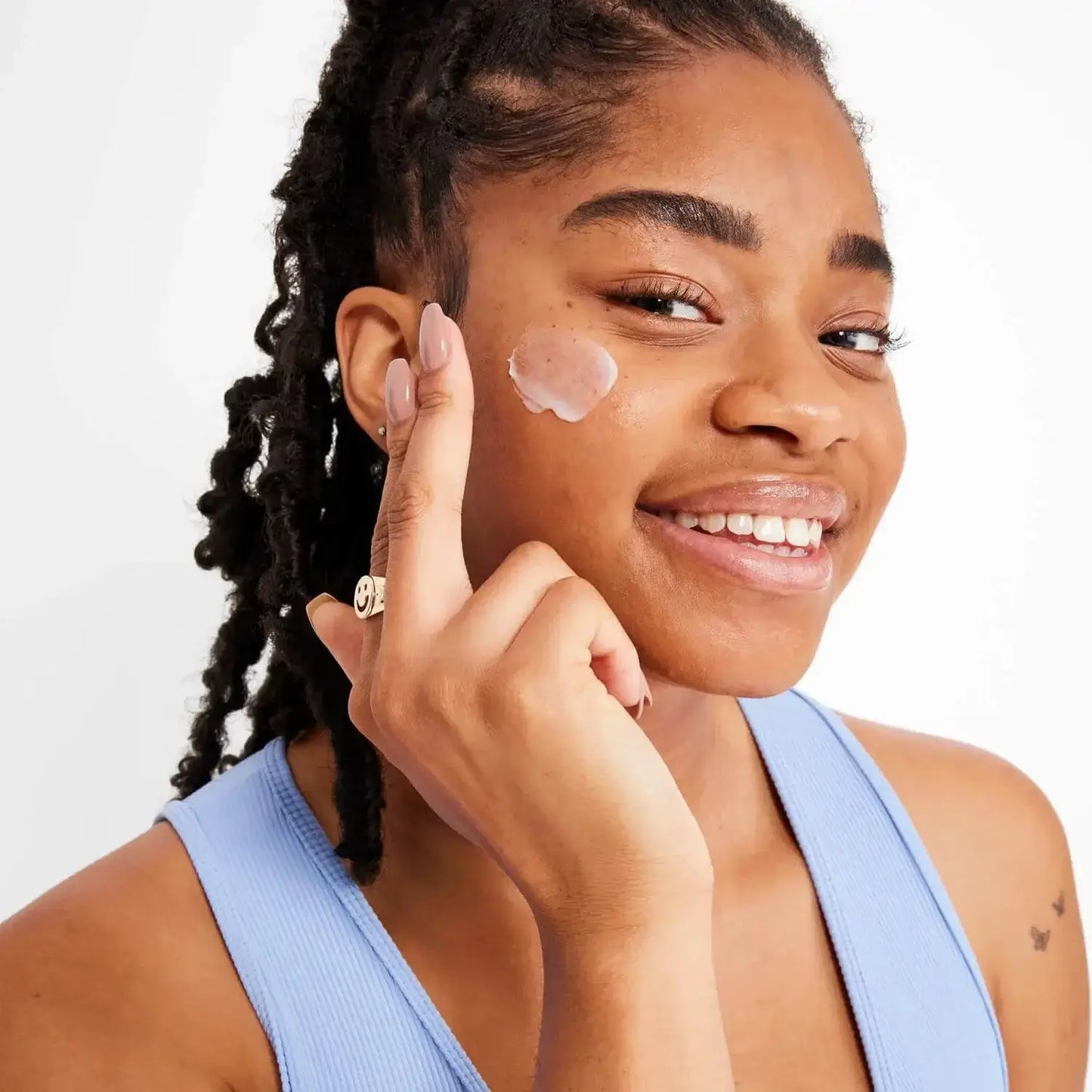 Smiling woman applying First Aid Beauty Ultra Repair Face Moisturiser 50ml on her cheek for instant hydration.