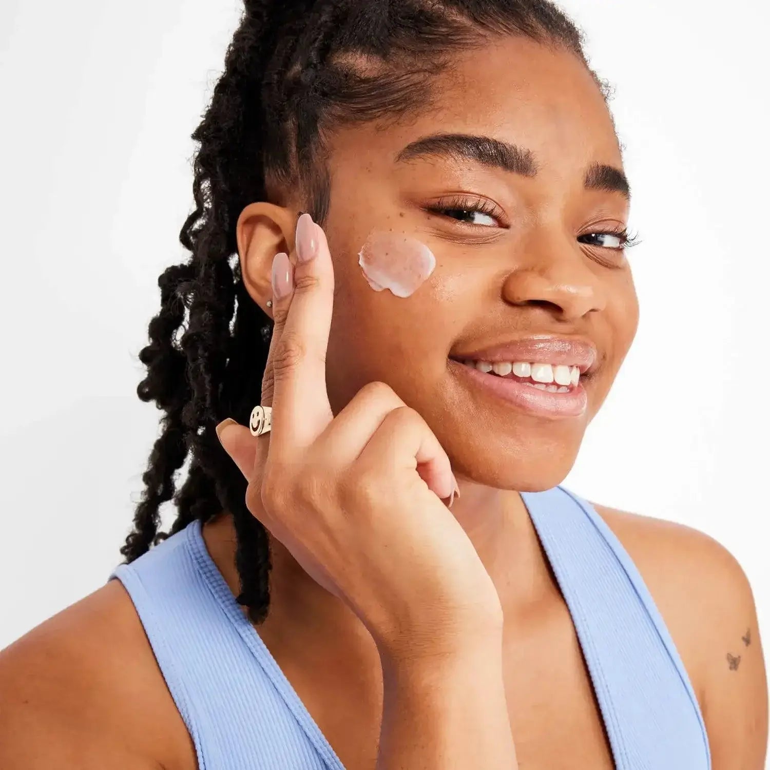 Smiling woman applying First Aid Beauty Ultra Repair Face Moisturiser 50ml on her cheek for instant hydration.