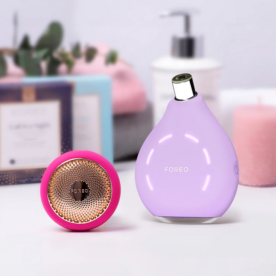 Two skincare devices, one pink and one purple, on a light surface with a blurred background.
