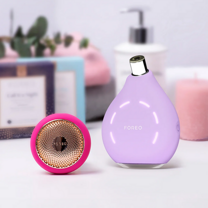 Two skincare devices, one pink and one purple, on a light surface with a blurred background.