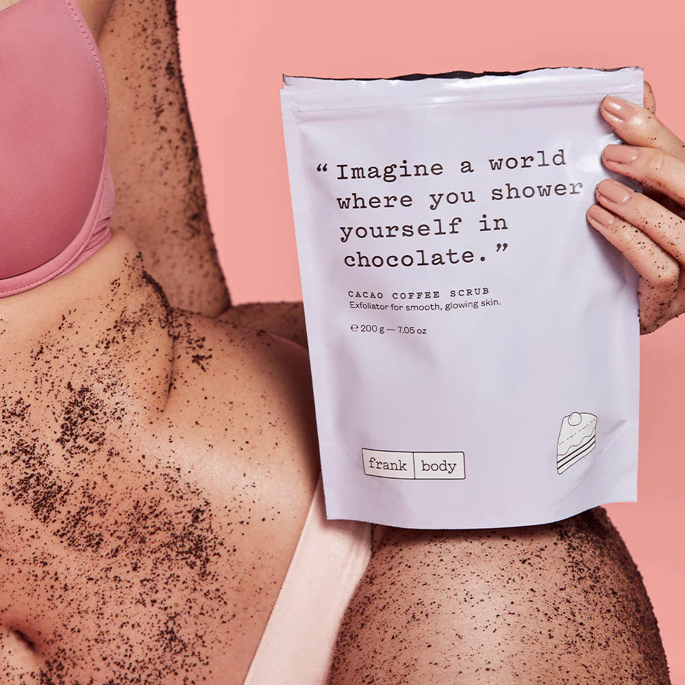 Person using a cacao coffee scrub with a package labeled 'frank body' on a pink background