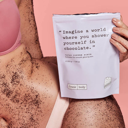 Person using a cacao coffee scrub with a package labeled 'frank body' on a pink background