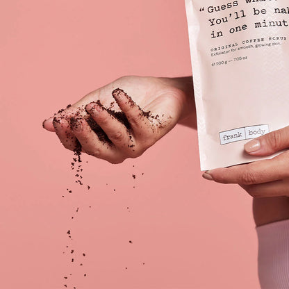 Hand holding coffee scrub with packaging labeled 'frank body' on a pink background
