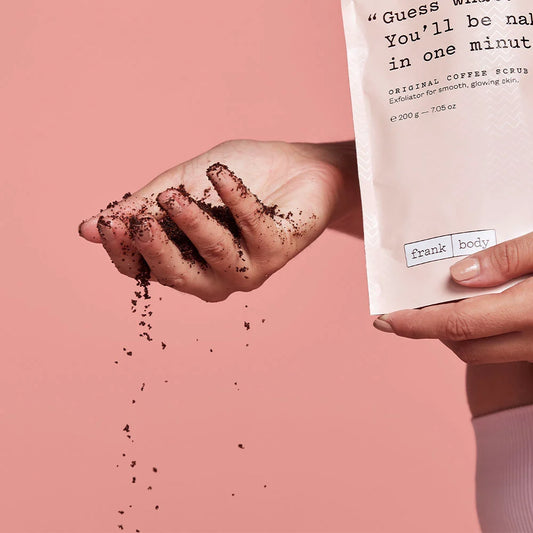 Hand holding coffee scrub with packaging labeled 'frank body' on a pink background