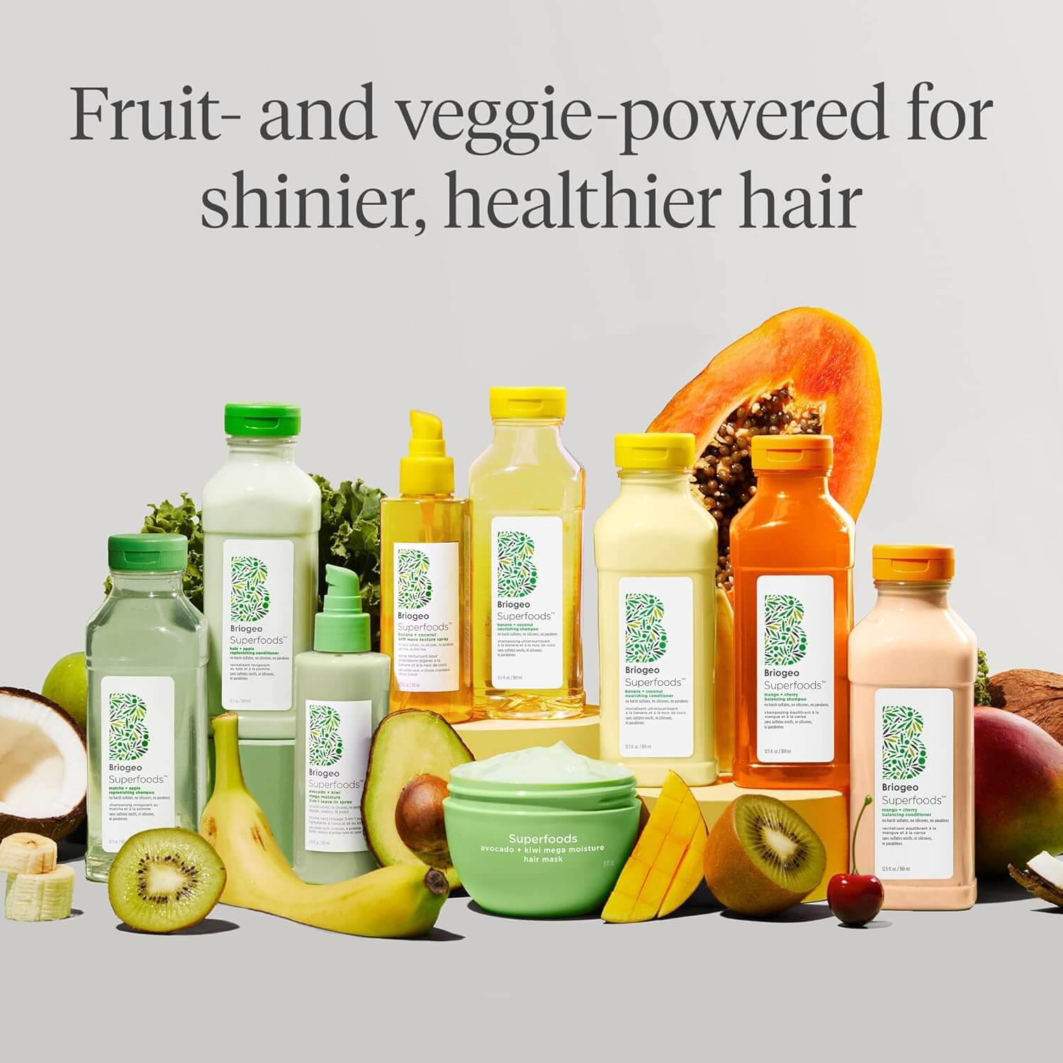 Collection of Briogeo hair care products with fruits and vegetables on a light gray background