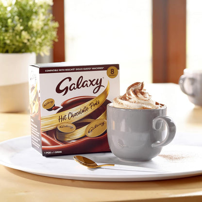 Box of Galaxy hot chocolate pods with a mug of hot chocolate on a table.