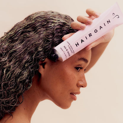 Person applying HAIR GAIN hair mask to their damp hair against a beige background