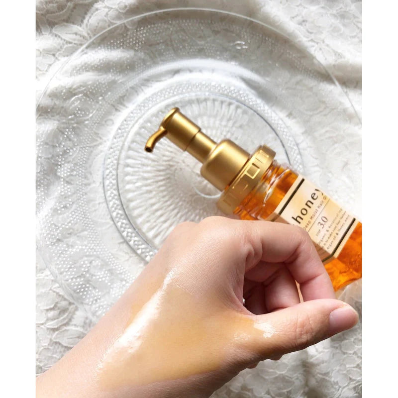 Hand holding a bottle of honey-based skincare product with a pump on a textured white background.