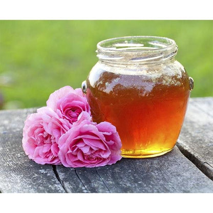 Jar of honey with pink roses on a wooden surface