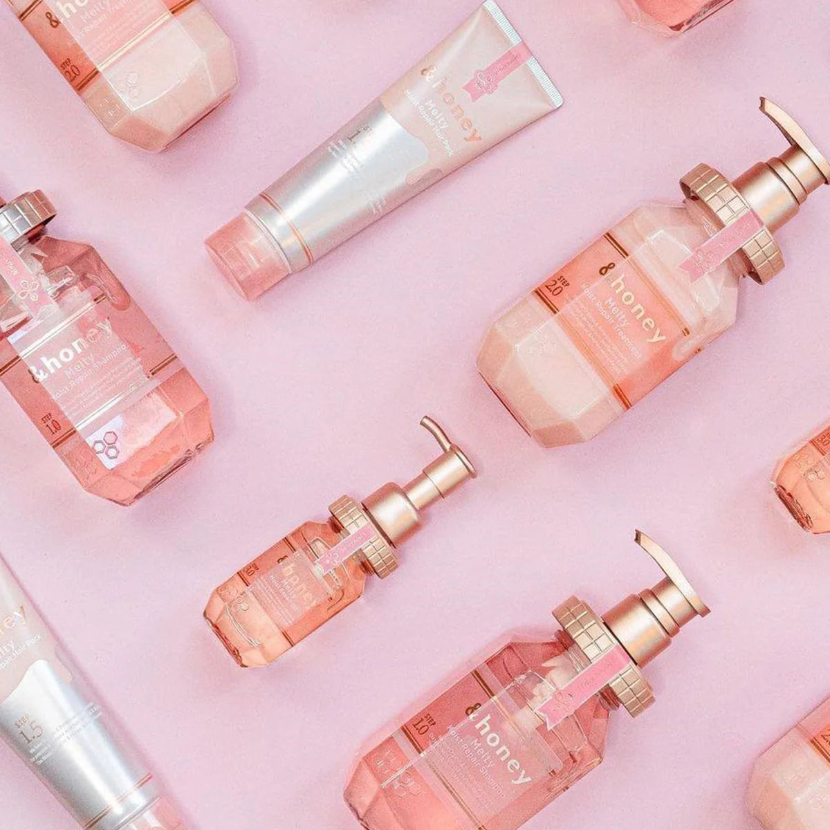 Various &honey hair care products displayed on a pink background, showcasing premium Japanese honey treatment.