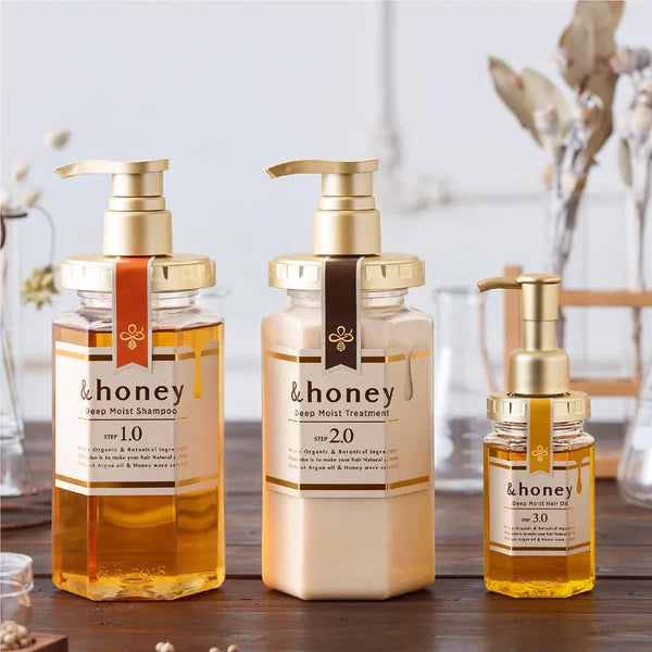 Three bottles of &honey shampoo and treatment on a wooden surface with a blurred background.