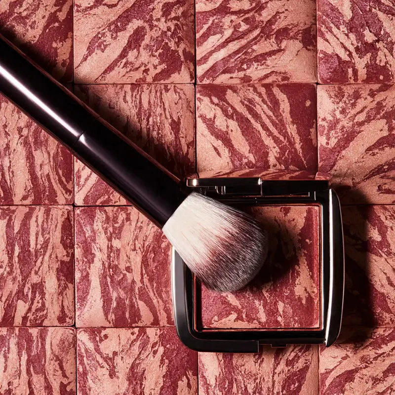 Hourglass Ambient Lighting Blush At Night showcased with a makeup brush on a marbled surface.
