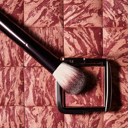 Hourglass Ambient Lighting Blush At Night showcased with a makeup brush on a marbled surface.