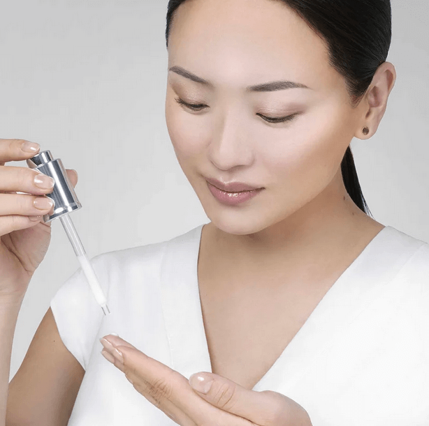 Woman applying Institut Esthederm Age Proteom Advanced Serum 30ml on her hand, showcasing skincare routine.