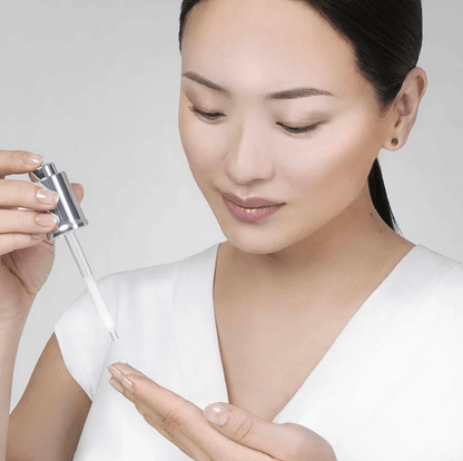 Woman applying Institut Esthederm Age Proteom Advanced Serum 30ml on her hand, showcasing skincare routine.