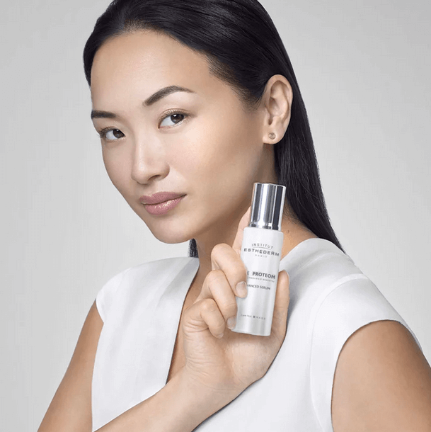 Institut Esthederm Age Proteom Advanced Serum 30ml held by a model, showcasing youthful glowing skin.