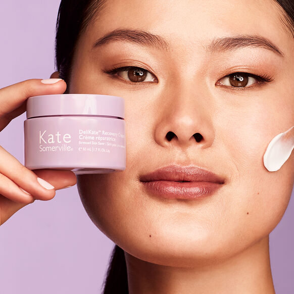 Woman applying cream to her face with a container of Kate Somerville product.