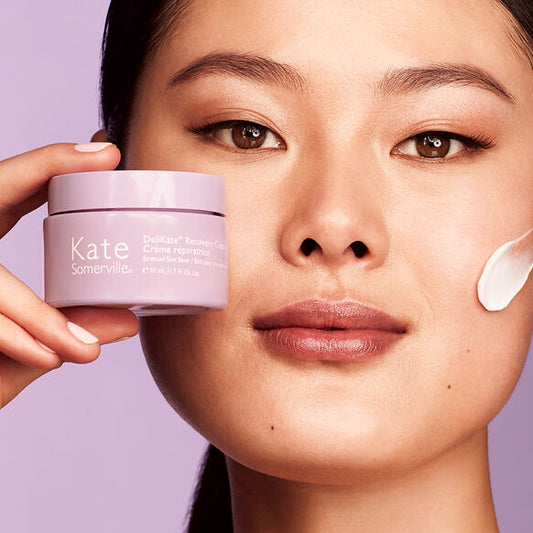 Woman applying cream to her face with a container of Kate Somerville product.