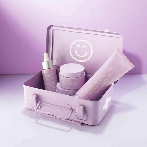 Set of Kate Somerville skincare products in a matching case with a smiley face logo on a light purple background.