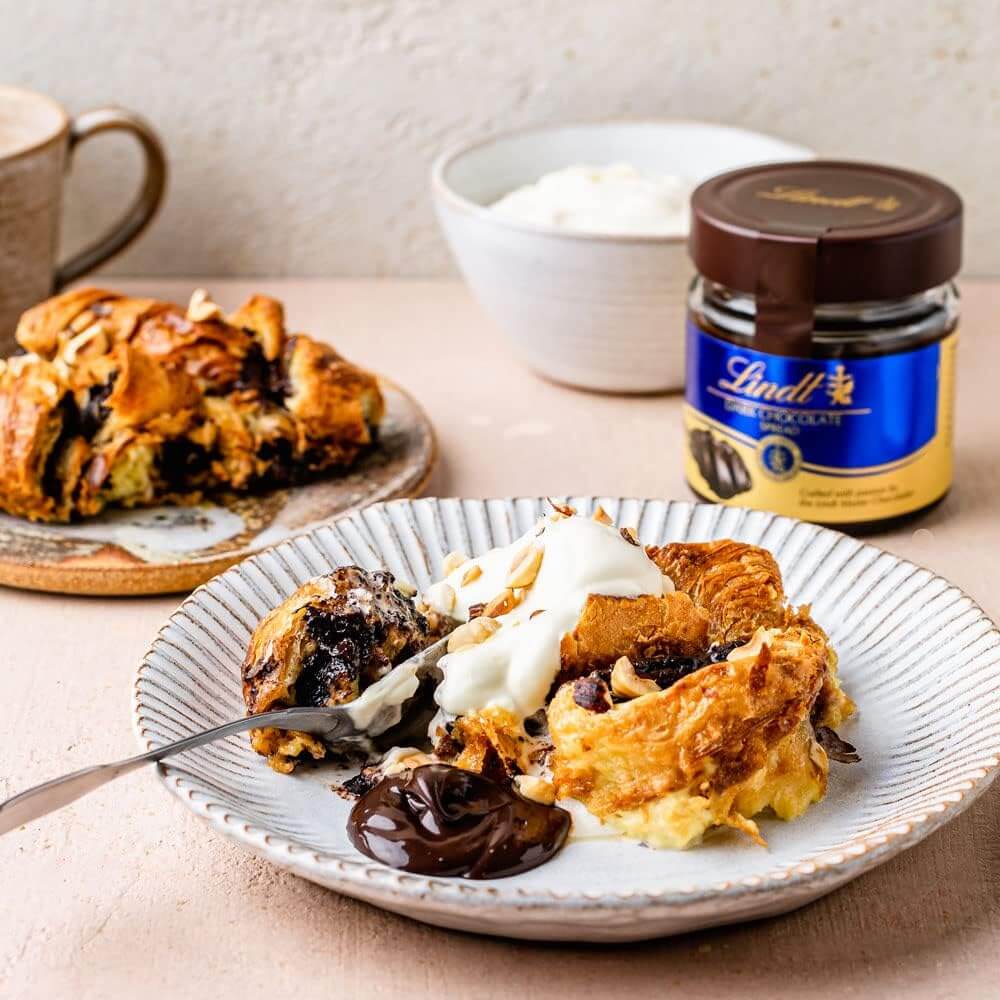 Dessert plate with croissants, whipped cream, and chocolate spread, with a jar of Lindt chocolate in the background.