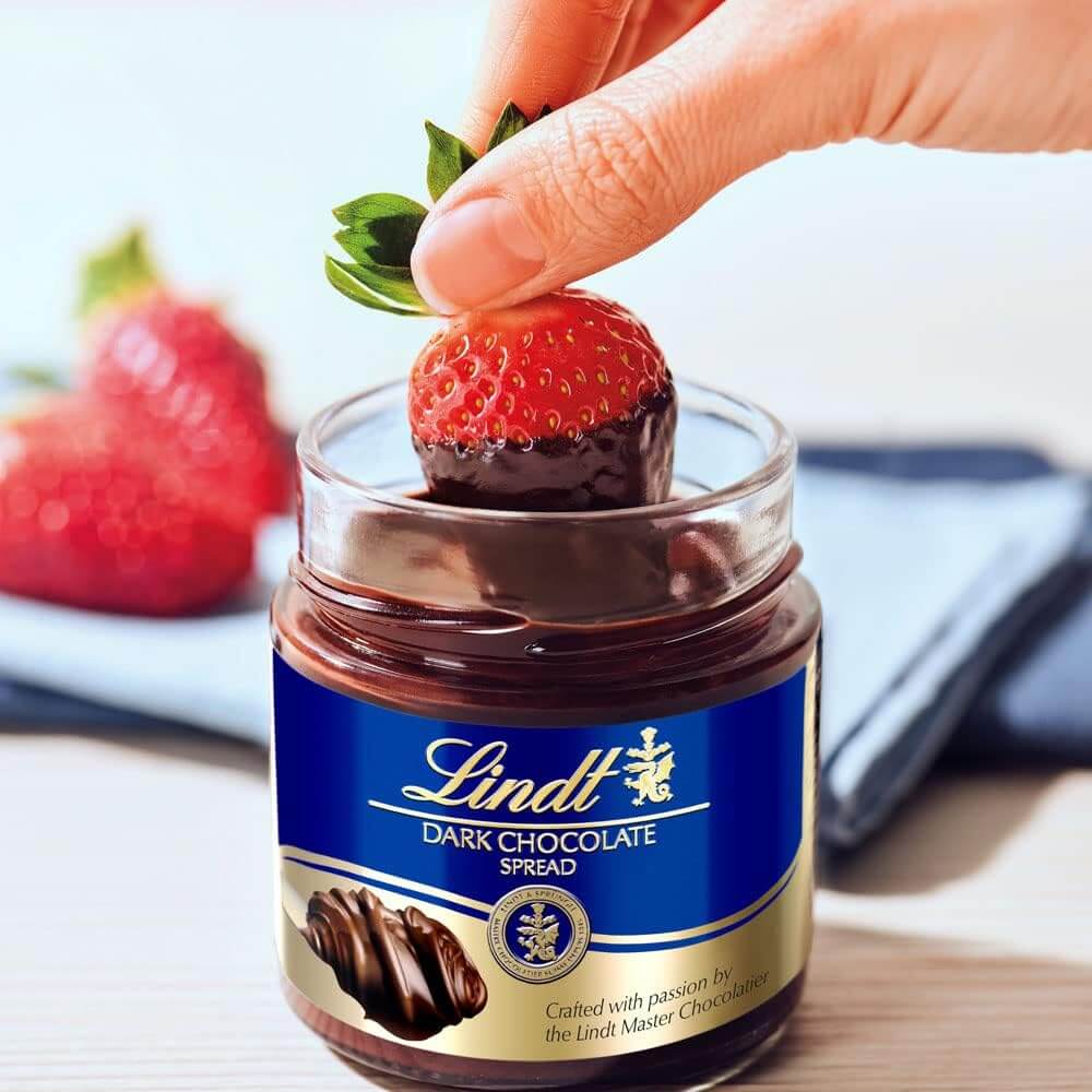 Lindt dark chocolate spread jar with a strawberry being dipped into it.