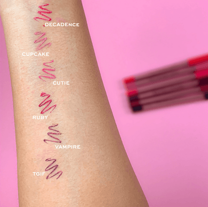 Revolution Color swatches on a person's arm with lip gloss names above them against a pink background.