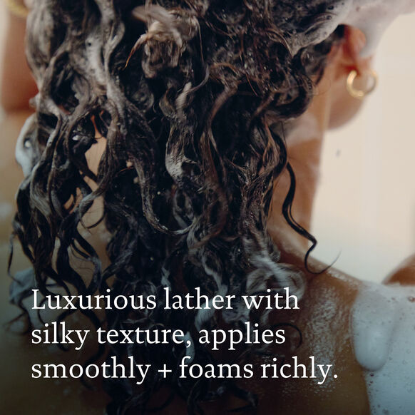 Person with wet, soaped hair and text describing the Living Proof shampoo's texture and application.
