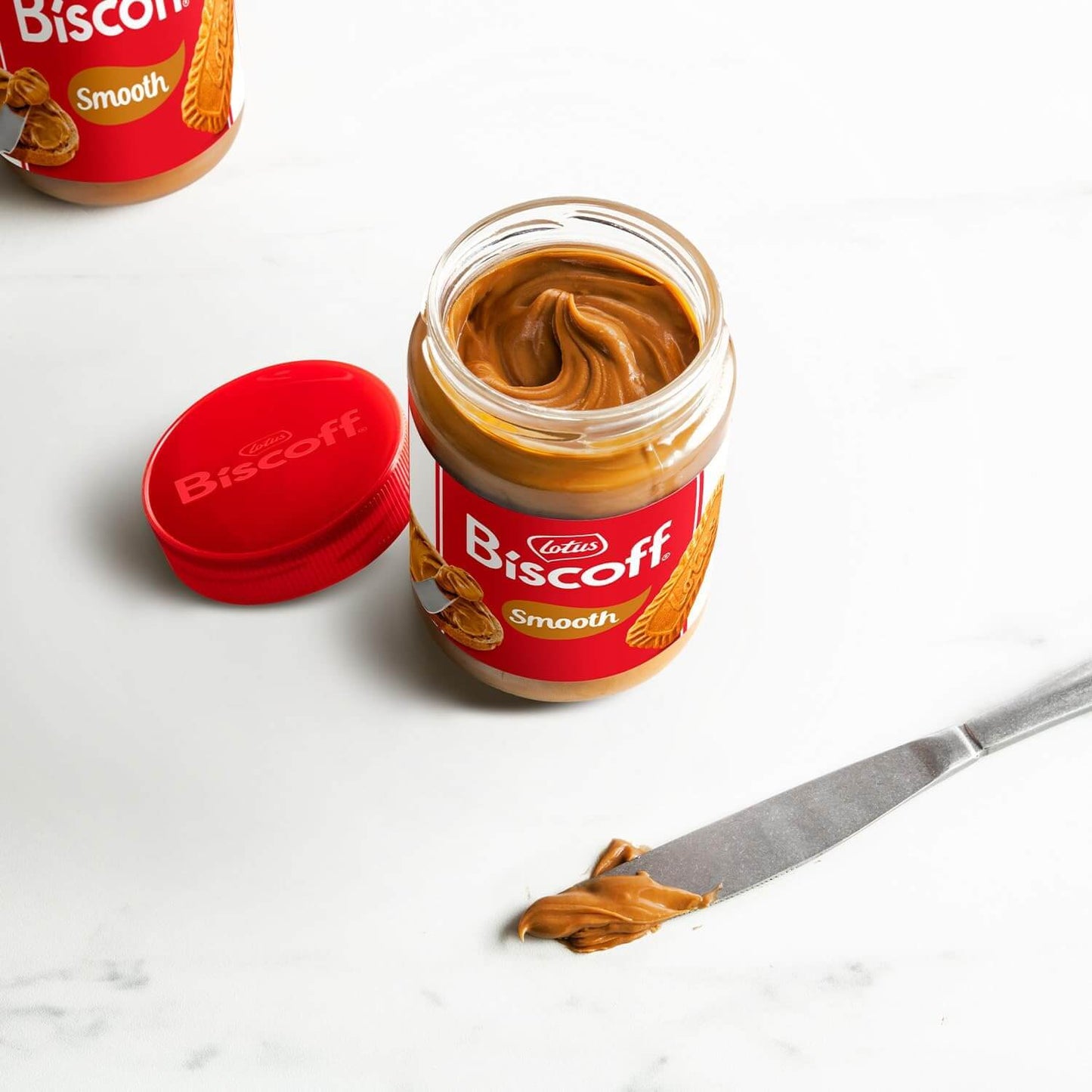 Jar of Lotus Biscoff spread with a knife and open lid on a white background