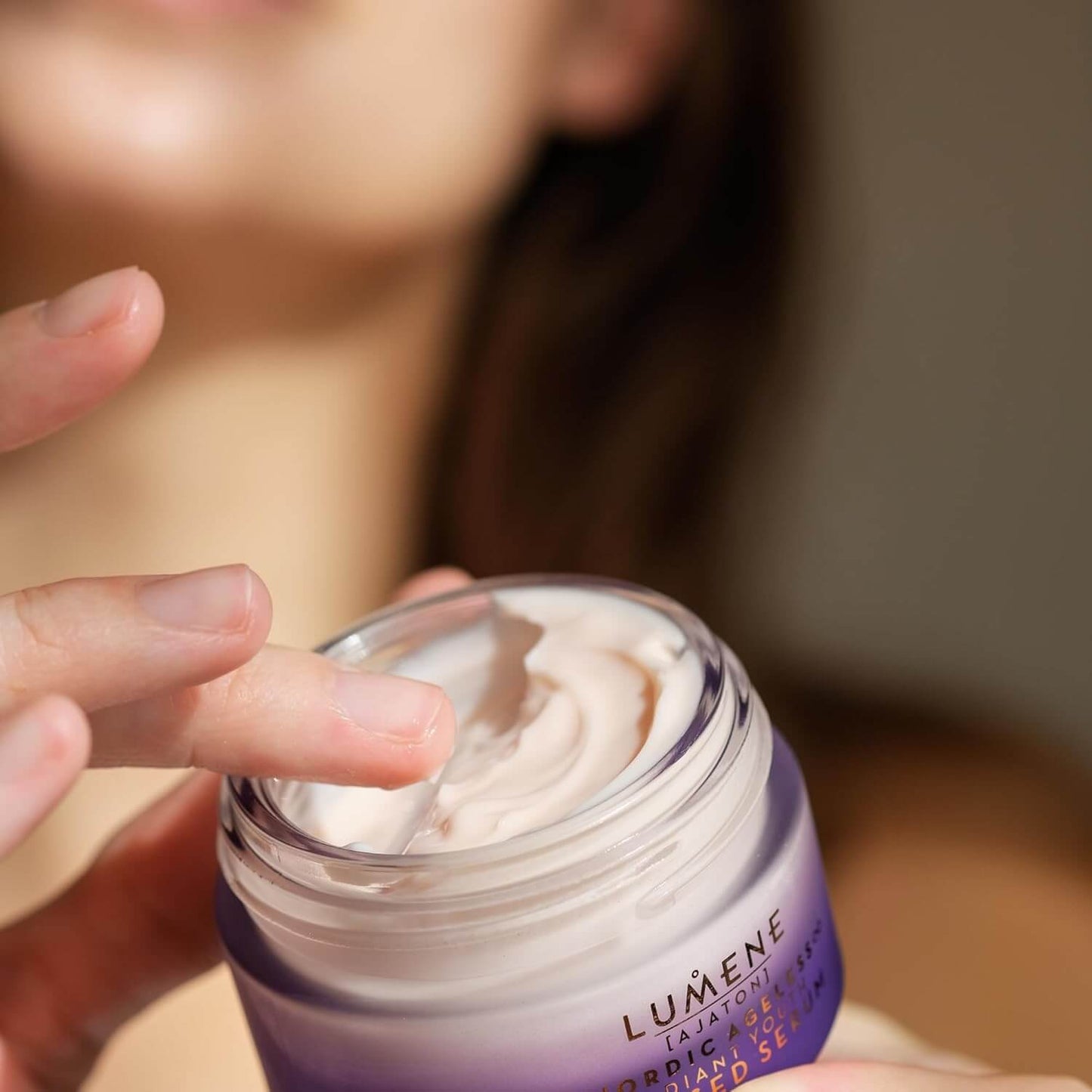 Person applying Lumene cream to their hand with a blurred background
