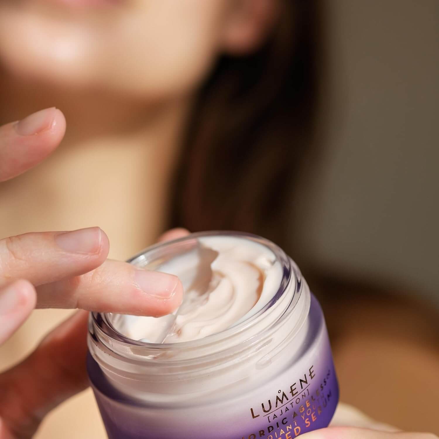 Person applying Lumene cream to their hand with a blurred background