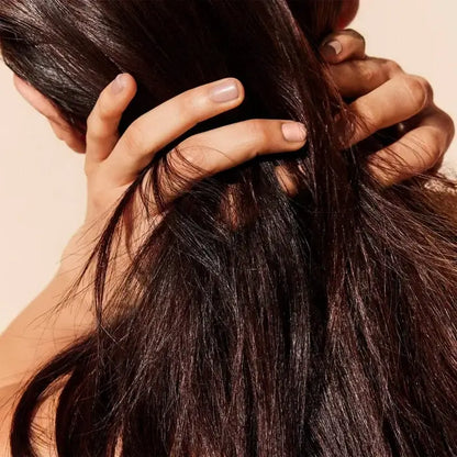 Close-up of a person's hand holding dark brown hair against a beige background Nuxe
