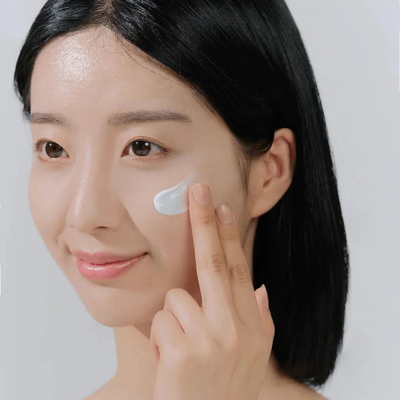 Woman applying cream to her face with a neutral background