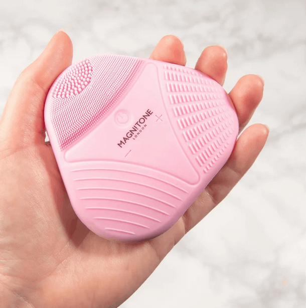 Magnitone XOXO SoftTouch Silicone Cleansing Brush in pink held in a hand, ideal for deep cleansing and skincare.