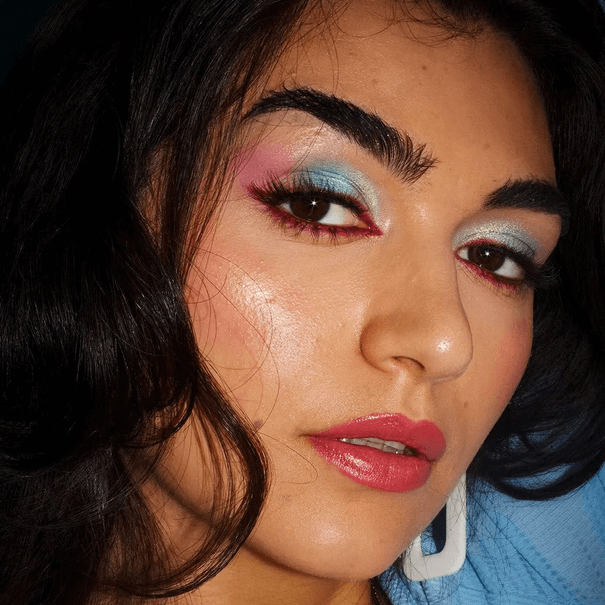 Close-up of a model showcasing vibrant blue and pink eyeshadow with bold eyeliner and glossy lips.
