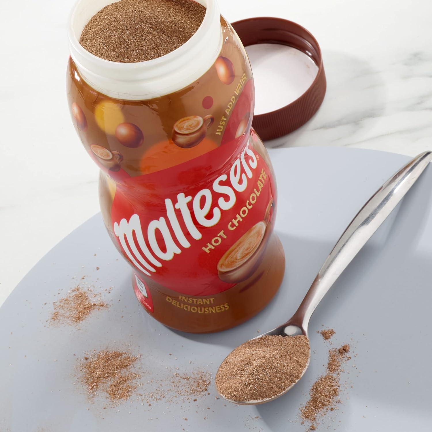 Maltesers hot chocolate mix jar with a spoonful of powder on a light surface
